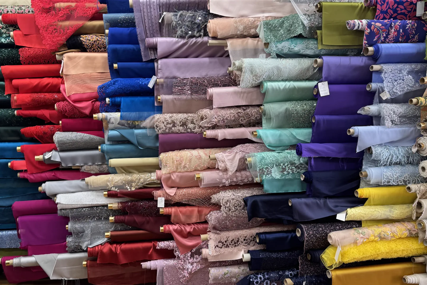 Rollos de telas apilados por colores: rasos, encajes y bordados en rojo, azul, rosa, morado y amarillo