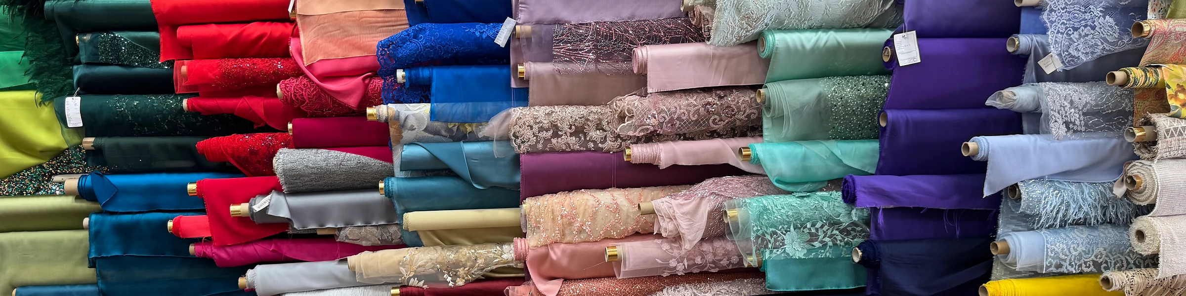 Rollos de tela apilados por colores: rasos, encajes y bordados en rojo, azul, rosa y verde