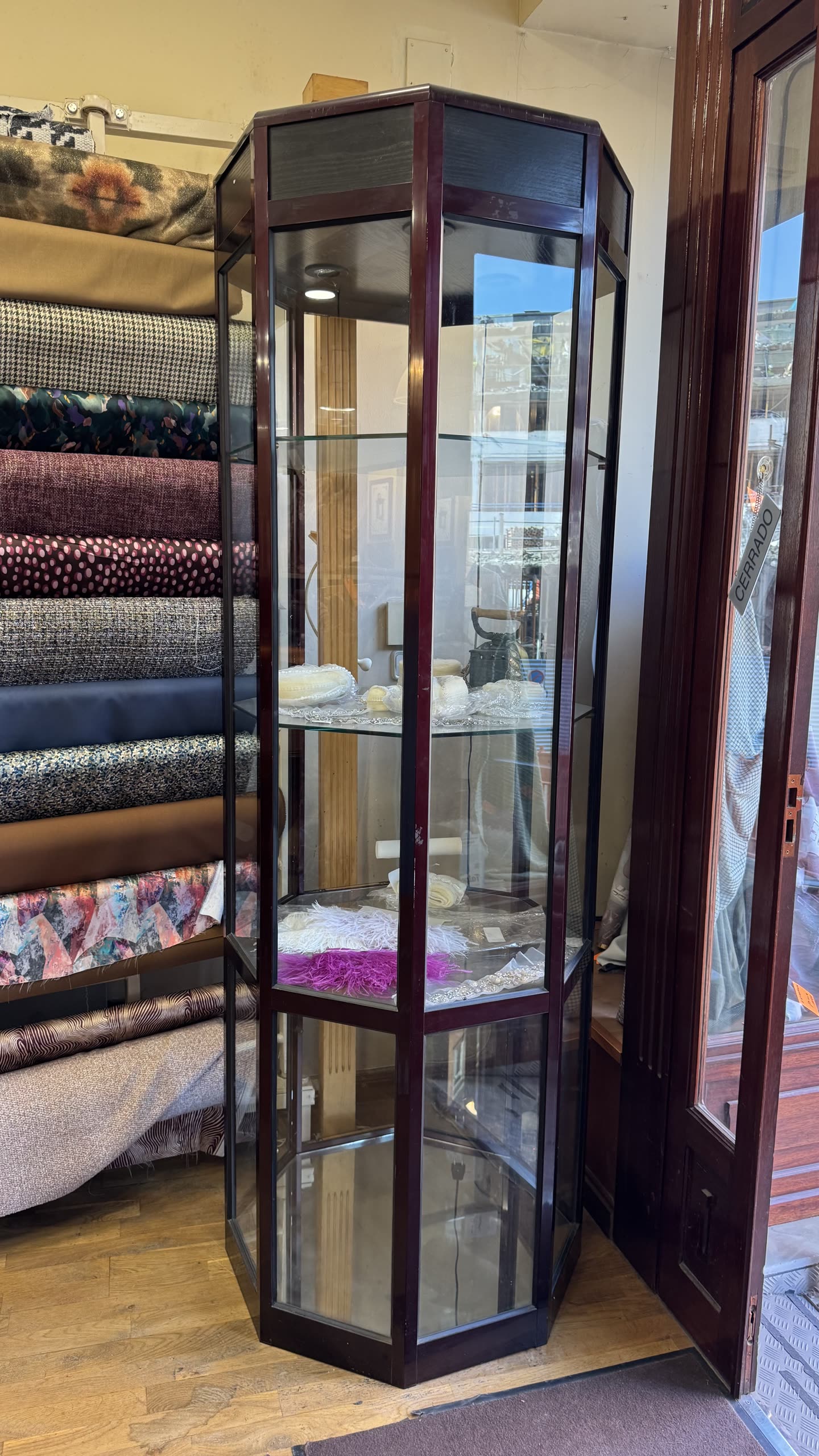 Vitrina hexagonal de cristal y madera oscura con telas y tocados